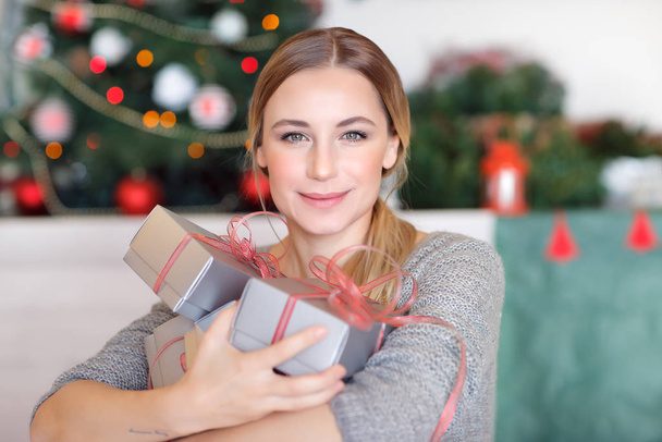 Portrait of a beautiful happy woman with gift boxes in hands sitting in a beautiful decorated room at home, happy Christmas holidays - Foto, Bild