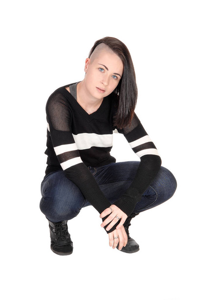 A pretty young woman in jeans and a sweater crouching on the floor.with a fancy haircut, isolated for white background. - Foto, imagen
