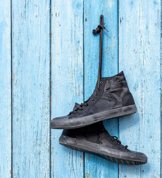black pair of worn men's textile sneakers hangs on the old  blue wooden background - Photo, Image