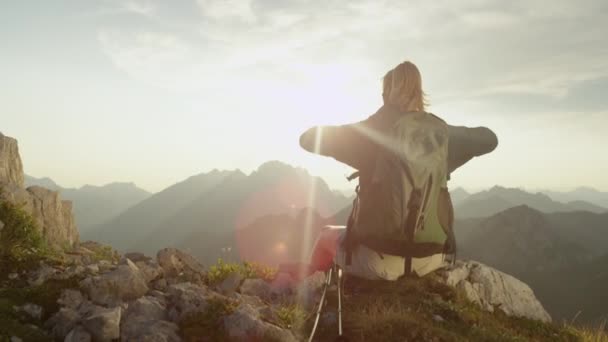 Yakından: tanınmayan kadın yürüyüşçü bir kayanın üzerinde oturur ve kollarını uzatır. - Video, Çekim
