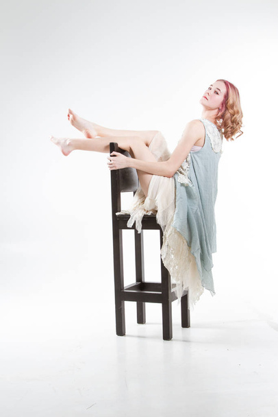 young girl is sitting on a high bar stool. Studio portrait on a white background - Фото, зображення