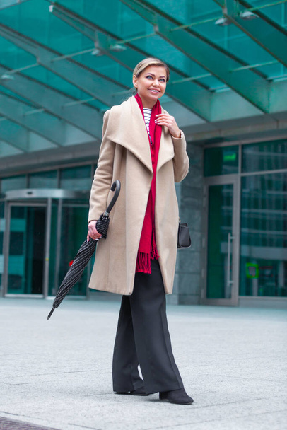 Outdoors lifestyle fashion portrait of stunning brunette girl. Walking on the city street. Going shopping. Wearing stylish white fitted coat, red neckscarf, black umbrella cane. Business woman. - Foto, immagini