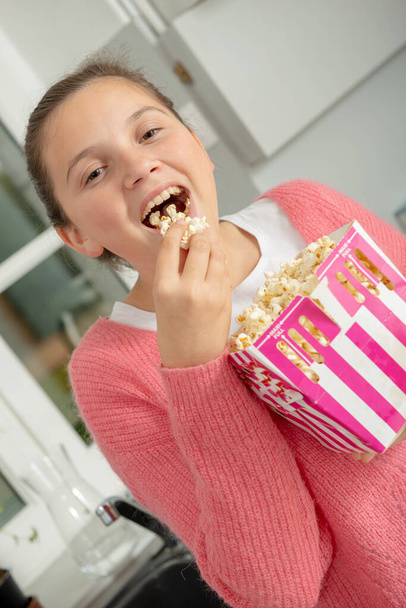 young teenage girl with a pink sweater eating popcorn at home - Fotoğraf, Görsel