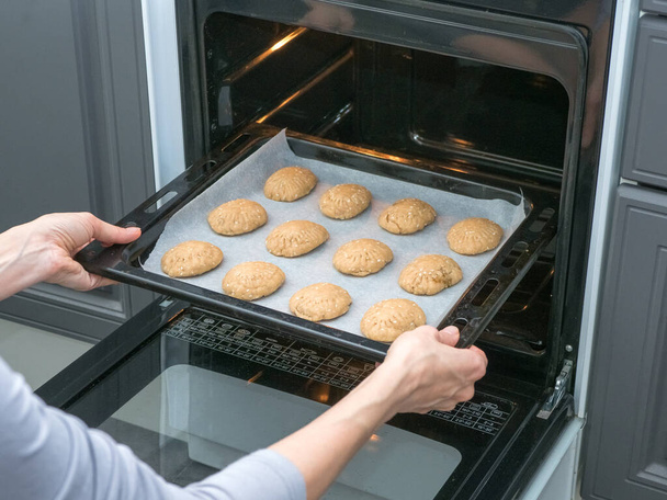El cocinero hornea galletas en el horno de la cocina. Hornear galletas de pan en el horno. Producción manual de cookies para las vacaciones
. - Foto, Imagen