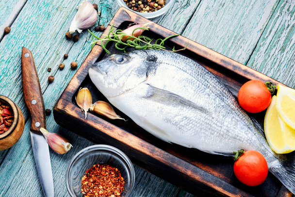 Fresh uncooked dorado or sea bream fish with herbs and spices on cooking board - Photo, Image