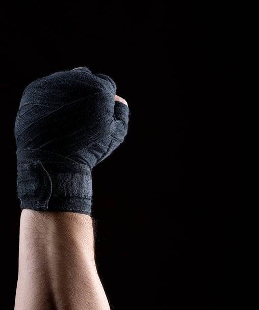 male right hand is wrapped in a black sports textile bandage on a black background, copy space - Valokuva, kuva