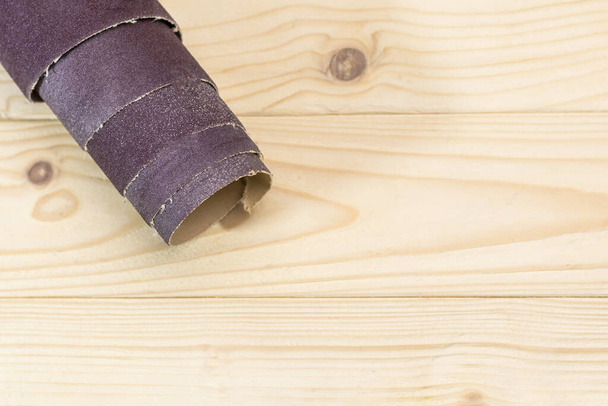 csiszolópapír tekercsbe csavarva fekszik egy fapadlón. Közelkép. Van egy árnyalat.. - Fotó, kép