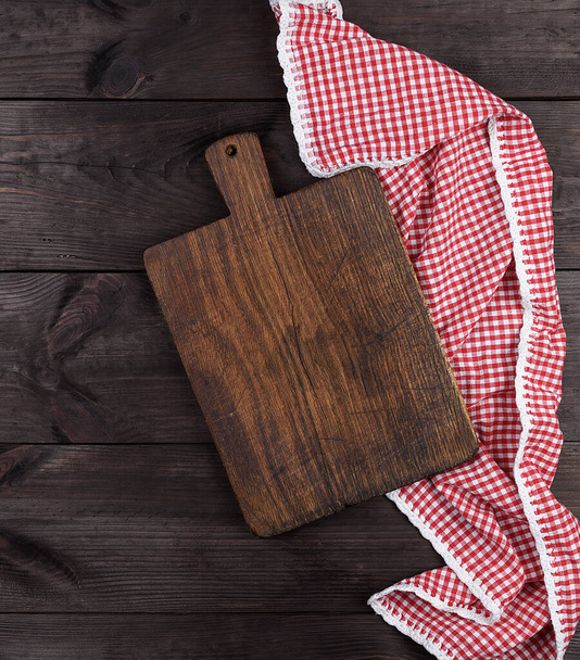 Empty very old wooden kitchen cutting board and a red towel on a brown table, the view from the top - Foto, Bild