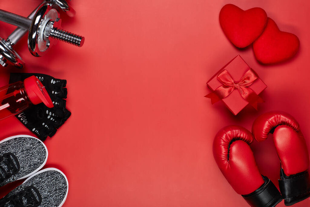 Dumbbells, boxing gloves, rope, bottle for water, gift box and two hearts on a red background.Top view with copy space. Valentine's Day card. Fitness, sport and healthy lifestyle concept. - Fotoğraf, Görsel