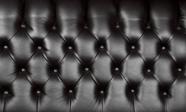 Background texture of black capitone genuine leather, retro Chesterfield style soft tufted furniture upholstery with deep diamond pattern and buttons, close up - Zdjęcie, obraz