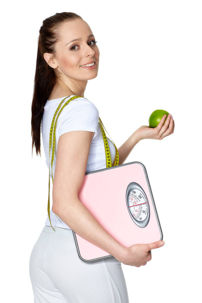 Sporty young woman with scales and apple on a white background.  Concept of healthy lifestyle. - Fotó, kép