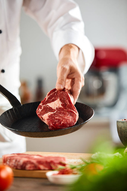 Séf kezében egy nyers, öreg marha steak felett egy kis vintage fekete serpenyő egy közeli a kezét - Fotó, kép