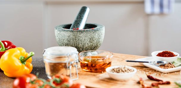 Stone pestle and mortar with oil and spices on a wooden kitchen board with selective focus - Fotografie, Obrázek