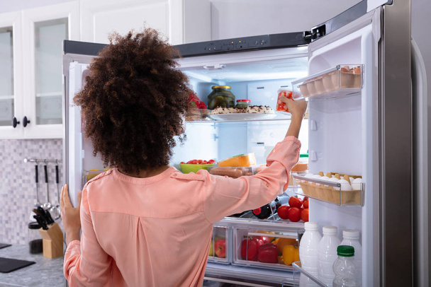 Rear View Of A Young Woman Taking Food To Eat From Refrigerator - Foto, imagen