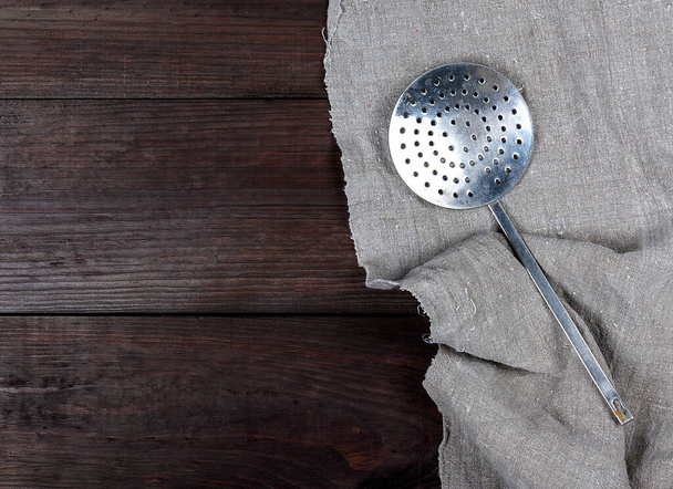 staré železo kuchyni skimmer na šedé lněný ubrousek, dřevěné hnědé pozadí, kopírování prostor - Fotografie, Obrázek