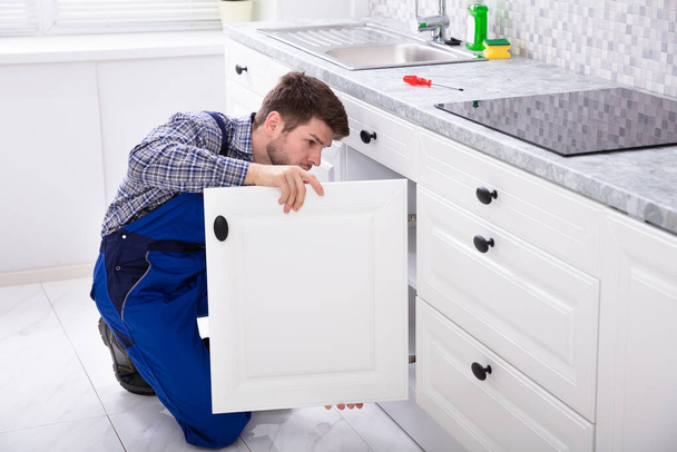 Crouching Repairman Fixing The Door Of Kitchen Sink - Foto, afbeelding