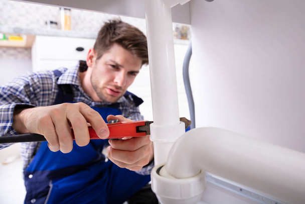 Young Male Plumber Repairing Sink Pipe With Adjustable Wrench - Valokuva, kuva