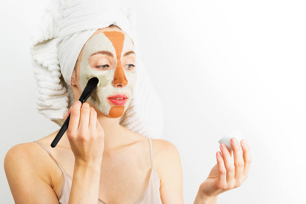 Beauty procedures skin care concept. Young woman applying facial gray and red mud clay mask to her face in bathroom. Woman with different masks on her face multi-masking - Fotó, kép