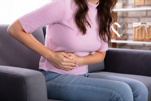 Mladá žena sedící na gauči trpí bolesti žaludku - Fotografie, Obrázek