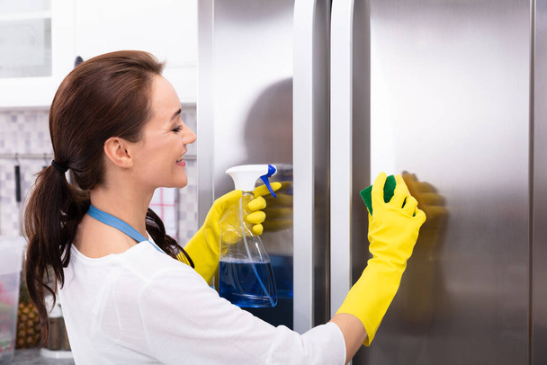 Happy Young Woman Cleaning Refrigerator With Sponge And Bottle Spray - Zdjęcie, obraz