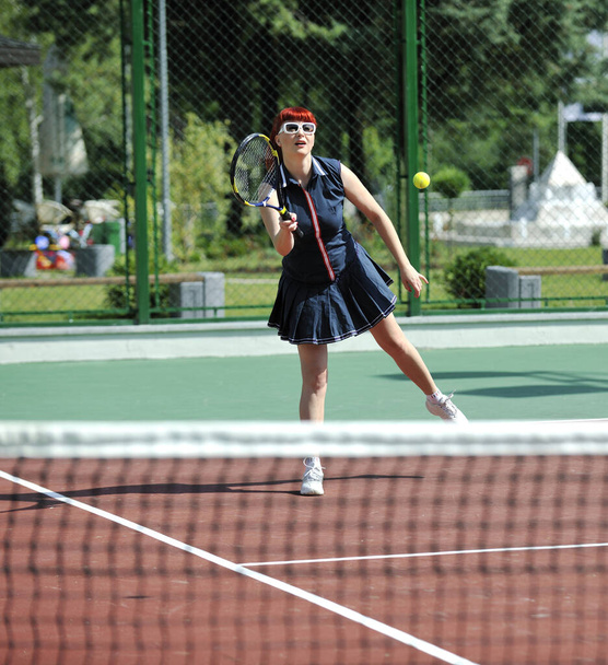 молода підтягнута жінка грає в теніс на відкритому повітрі на помаранчевому тенісному полі рано вранці
 - Фото, зображення