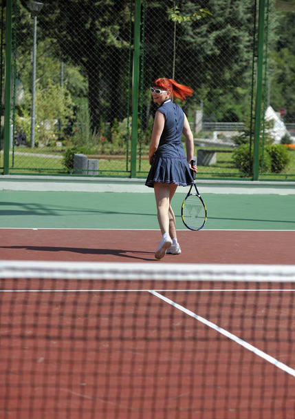 junge fitte Frau spielt Tennis im Freien auf orangefarbenem Tennisplatz am frühen Morgen - Foto, Bild