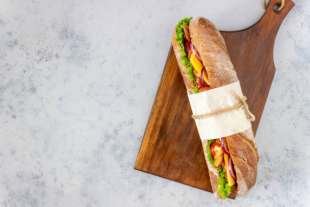 Un sándwich de pan negro con ensalada, tocino, tomate, queso y cebolla. El desayuno. Comida rápida
. - Foto, Imagen