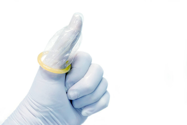 Kciuk i prezerwatywa w ręce lekarza na białym tle. - Zdjęcie, obraz
