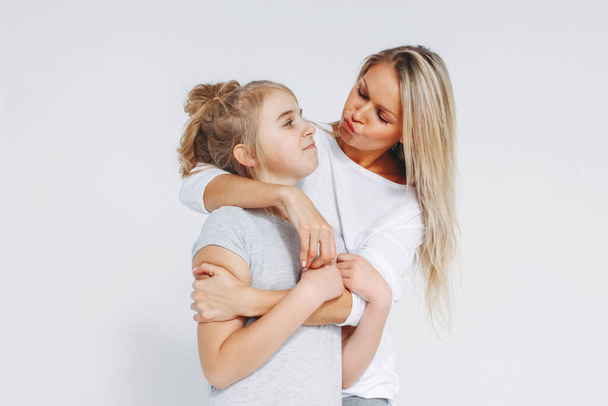 Beautiful blonde mom and daughter preteen in pajamas hugging and having fun isolated on white background - Photo, Image