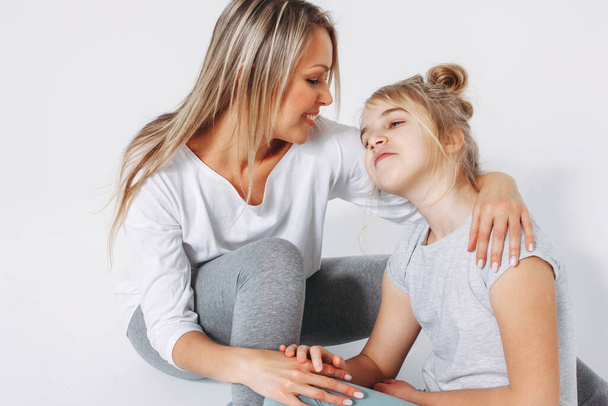Beautiful blonde mom and daughter preteen in pajamas sitting and hugging isolated on white background - Photo, Image