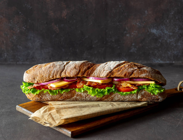 A sandwich of dark bread with salad, bacon, tomatoes, cheese and onions. Breakfast. Fast food. - Foto, Bild