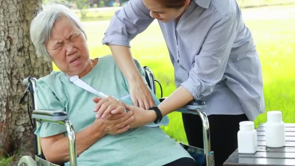 Τραυματισμένη Ασιάτισσα ηλικιωμένη γυναίκα με υποστήριξη αγκώνα που πάσχει από αρθρίτιδα, πονόλαιμο, πόνο στον αγκώνα, ασθένεια των αρθρώσεων ή μυοσίτιδα, δυστυχισμένη ηλικιωμένη γυναίκα με προστατευτικά αγκώνων που κάθεται σε αναπηρική καρέκλα  - Πλάνα, βίντεο