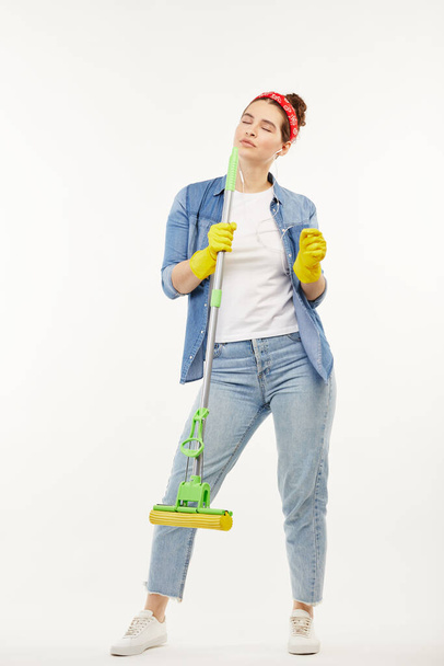 Pretty woman in work-wear holds a green mop and dances. - Fotoğraf, Görsel