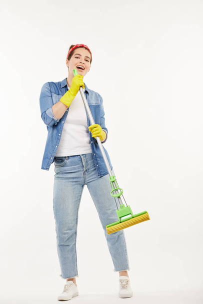 Pretty woman in work-wear holds a green mop and sings. - Φωτογραφία, εικόνα