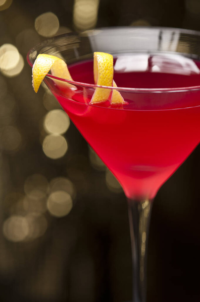 Cosmopolitan cocktail with lemon garnish in front of a gold glitter background - Foto, afbeelding
