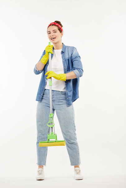 Pretty woman in work-wear holds a green mop and dances. - Φωτογραφία, εικόνα