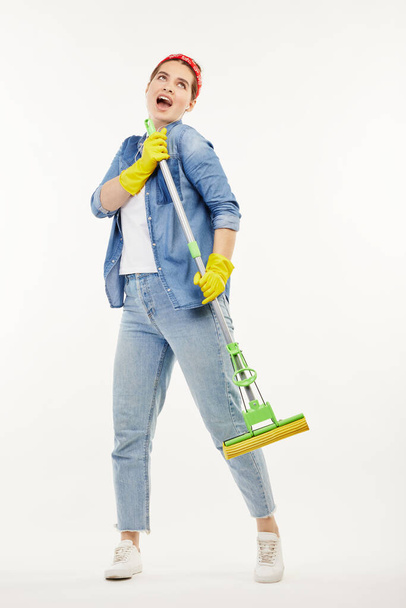 Pretty woman in work-wear holds a green mop and sings. - Photo, image