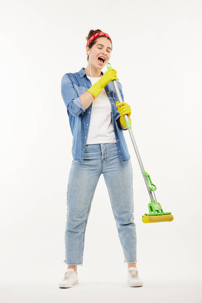 Pretty woman in work-wear holds a green mop and sings. - Фото, изображение