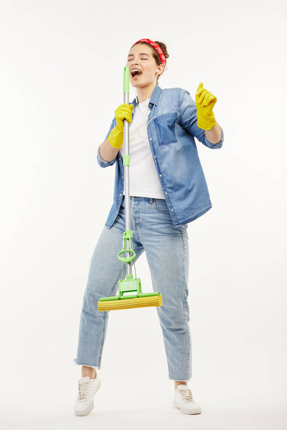 Pretty woman in work-wear holds a green mop and sings. - Фото, зображення