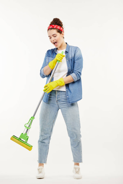 Pretty woman in work-wear holds a green mop and dances. - Fotoğraf, Görsel