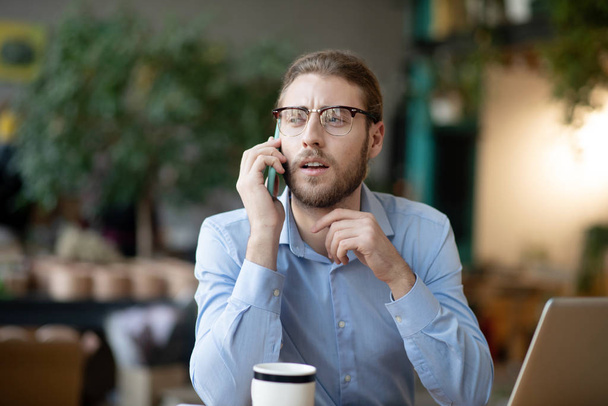 Young businessman in glasses talking positively on a smartphone. - Fotografie, Obrázek