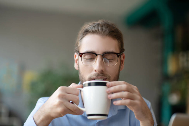 Jovem com óculos olhando sorrindo para uma xícara de café
. - Foto, Imagem