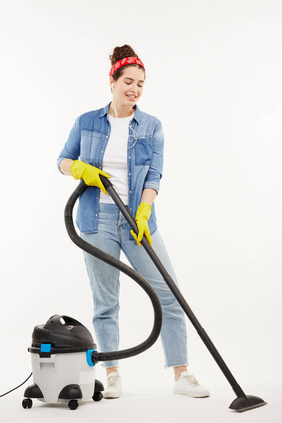 Pretty woman in work-wear uses a big wacuum cleaner. - Zdjęcie, obraz