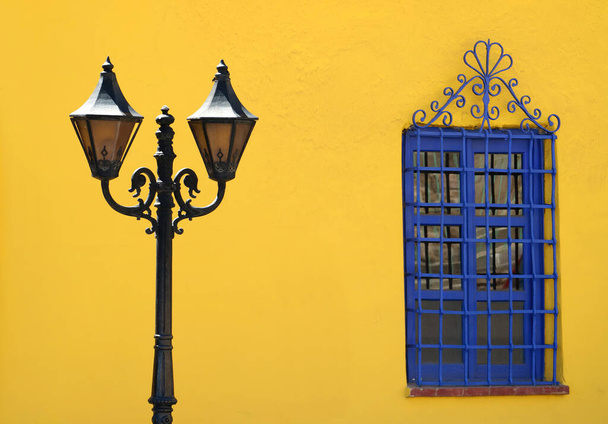 Lampe de rue magnifique de style vintage contre un mur rugueux jaune vif avec une fenêtre artistique bleue vibrante
 - Photo, image
