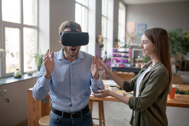 Woman assisting man while he is using VR glasses - Foto, afbeelding