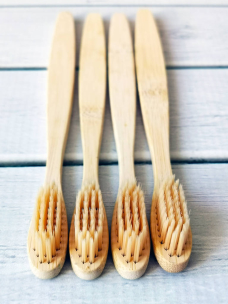 A family set of four wooden toothbrushes on white wooden background with copy space  - Zdjęcie, obraz