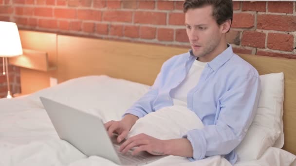 Young Man Celebrating Success on Laptop in Bed - Filmagem, Vídeo
