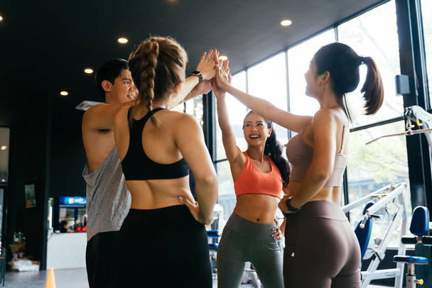 Smile man and women making hands together in fitness gym. Group of young people doing high five gesture in gym after workout. Happy successful workout class after training. Teamwork concept. - Photo, Image