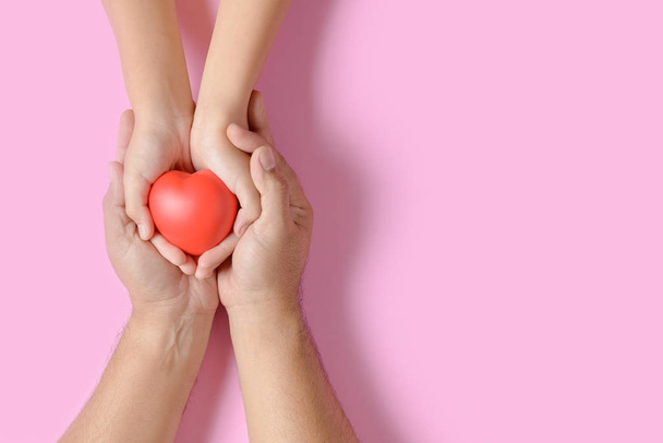 mãos de adulto e criança segurando coração vermelho isolado em rosa
 - Foto, Imagem