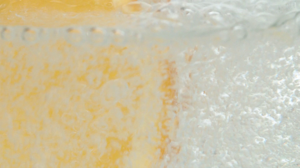 Mineraal bruisend water dat in een glas met een schijfje sinaasappel wordt gegoten. Extreme close-up natuurlijk koolzuurhoudend mineraalwater op witte ondergrond. Langzame beweging - Video